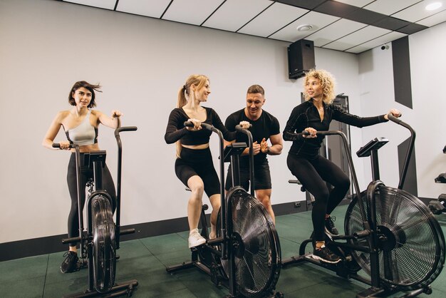 Young women make exercising on air bikes at gym with trainer motivating