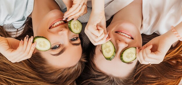 Le giovani donne fanno la maschera di bellezza viso fatta in casa con fette di cetriolo