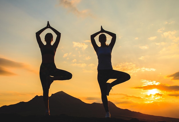 Young women practicing yoga at sunset in beautiful mountain location.
