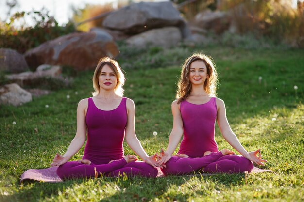 Young women in purple sports wear exercising together on the grass