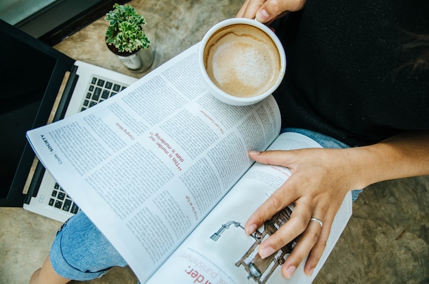 Photo young women reading a book and holding cup of coffee