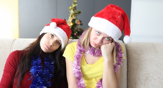 Young women in santa claus hat are boring on sofa at home