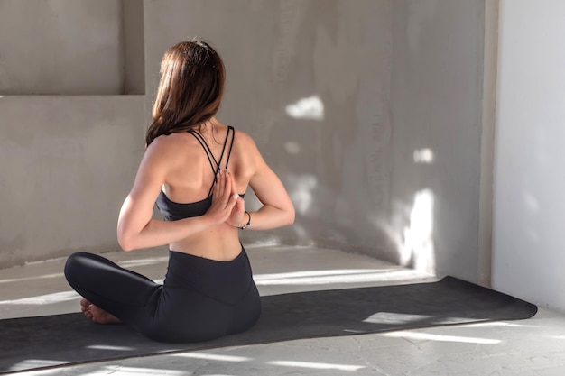 Young women sits on yoga mat and meditating with hands clasped behind her back