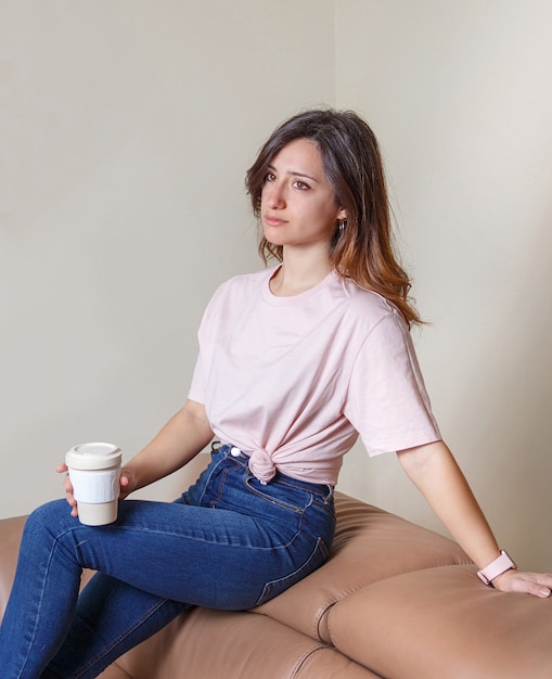 Young women sitting on the sofa at home with coffee to  go