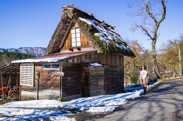 Young Women stand with Heritage Wooden Farmhouse in Japan's famous village.