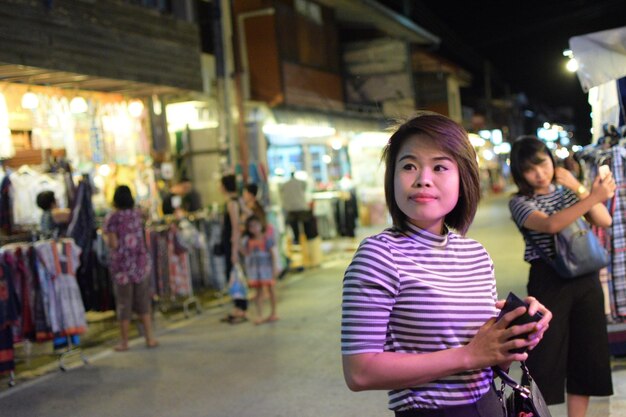 写真 夜照らされたストリートマーケットに立っている若い女性