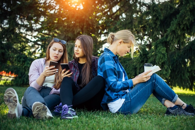 Young women students on the green grass among the trees