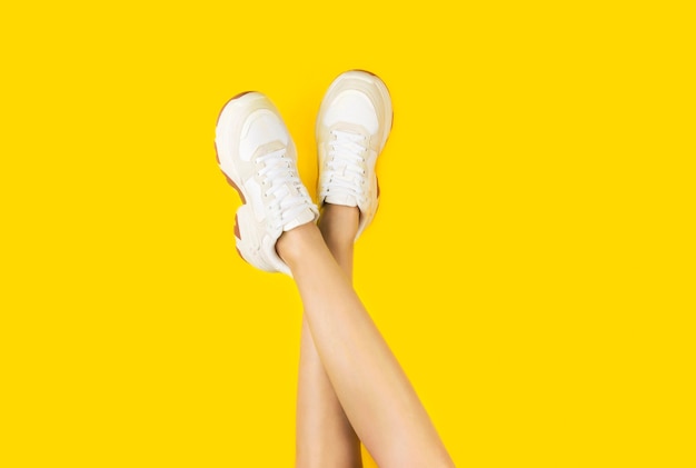 Young women in stylish sneakers on a yellow background.