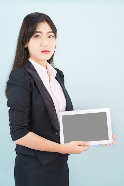 青い背景に立っている彼女のデジタルタブレットを保持しているスーツの若い女性