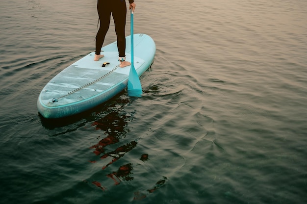 Молодые женщины в термоодежде гребут веслом на доске для серфинга на фоне пляжной доски и концепции длинной доски