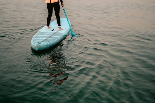 Young women in thermo clothing rowing oar on sup board paddleboard background of beachSup board