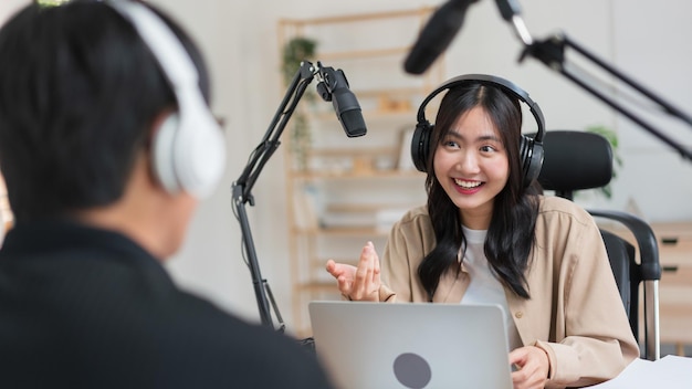 Young women using laptop and microphone to interviewing man guest and recording for audio podcast