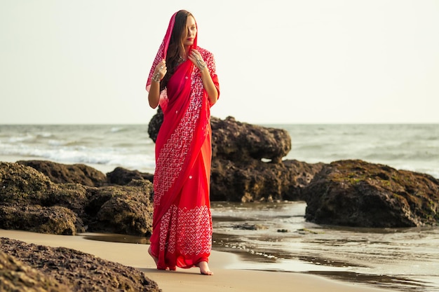 Giovani donne che indossano un sari rosso sulla spiaggia goa india.girl in sari indiani tradizionali sulla riva di un'isola paradisiaca tra le rocce e la sabbia che si godono la libertà e il tramonto