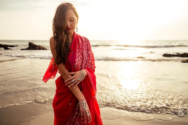 Young women wearing a red saree on the beach goa India.girl in traditional indian sari on the shore of a paradise island among the rocks and sand enjoying the freedom and the sunset