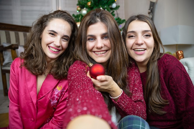 Молодые женщины с рождественскими безделушками сидят дома и счастливо делают селфи