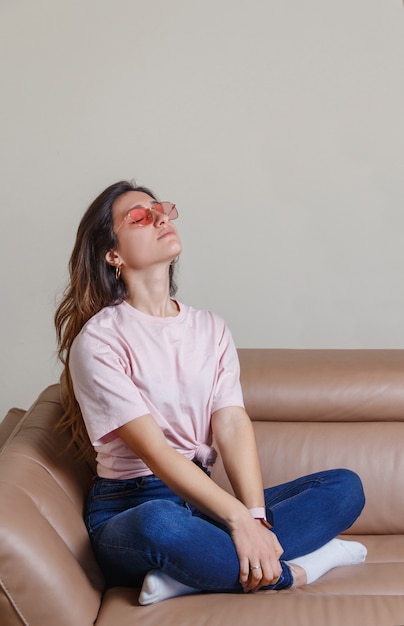 Young women with pink glasses sitting on the sofa at home with her eyes closed