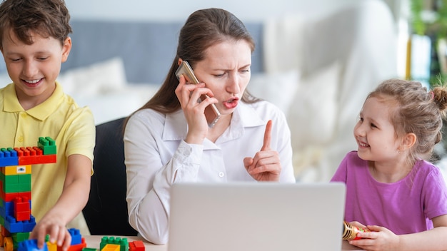 Young women works at home with laptop, along with children. Children make noise