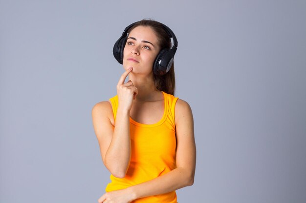 Young wondering woman in yellow Tshirt listening to the music in black headphones in studio
