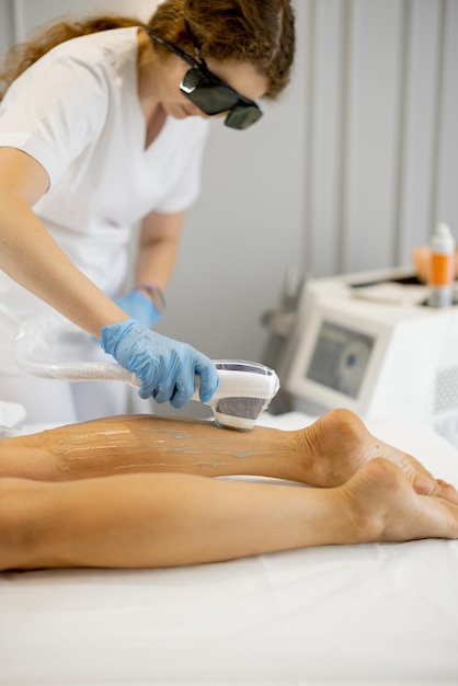 Young worker of a beauty salon during hair removal procedure on a woman's legs Depilation concept and beauty procedures