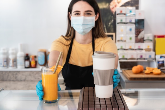 Young worker delivering takeaway order to customer inside restaurant while wearing face mask