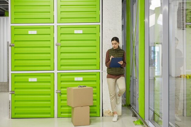 Photo young worker making notes in document she registrating parcels before delivery in warehouse