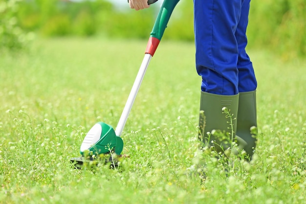 Young worker mowing lawn with grass trimmer outdoors on sunny day closeup