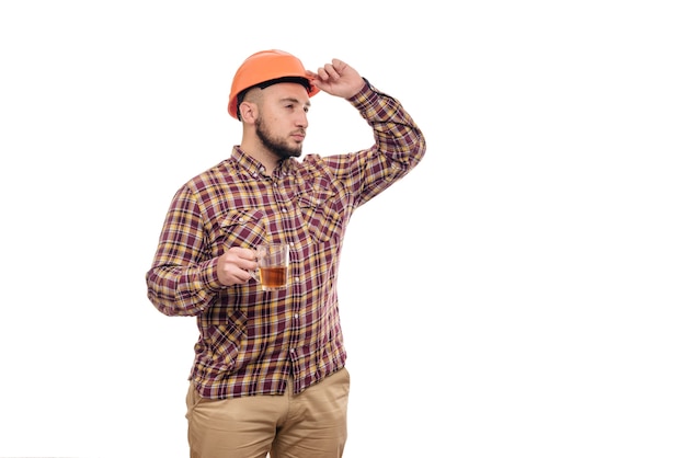 Young worker in an orange helmet holds a cup of tea, isolated white background