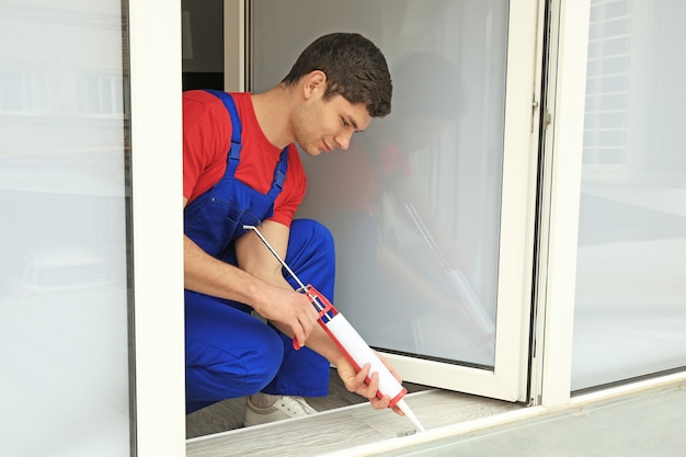 Young worker sealing joints of window in office