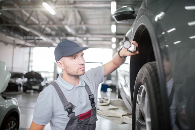 Young worker stands close to car and hold lights. He is serious and concentrated.