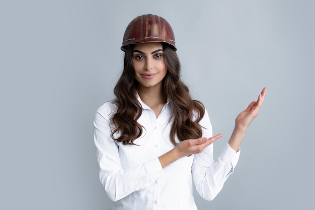 Young worker woman in helmet pointing on copy space on gray background