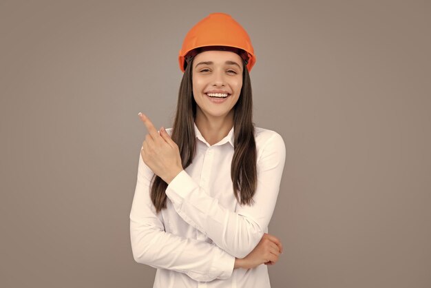 Young worker woman in helmet pointing on copy space on gray\
background