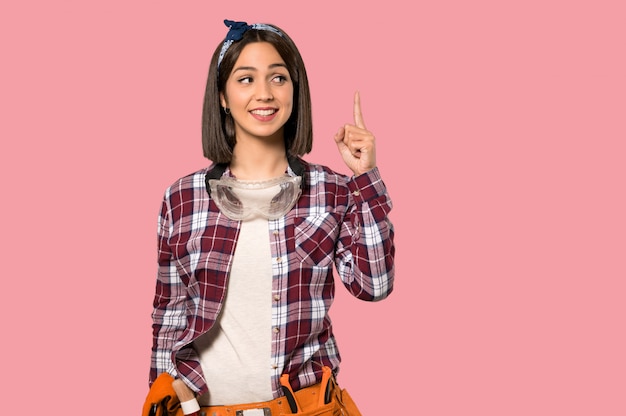 Young worker woman intending to realizes the solution while lifting a finger up on isolated pink wall