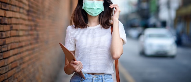 Photo young working asian woman wear surgical mask with tablet at thapae gate landmark of chiang mai province, thailand