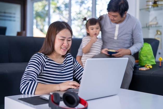 若い働く母親は、娘が横で遊んでいる間、自宅で仕事をしています