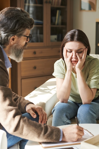 心理学者の若い心配している女性患者は、彼女の恐れや他の問題について専門家に話している間、彼女の顔に触れています