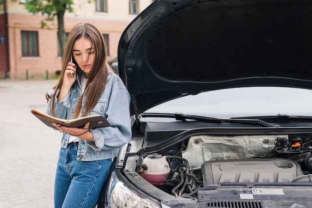 車の避難を呼びかけている心配している若い女性が道路で故障した。女性は故障した車の保険サービスを呼び出します。