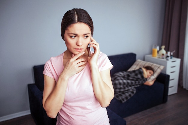 Young worried woman stand in room and talks on phone