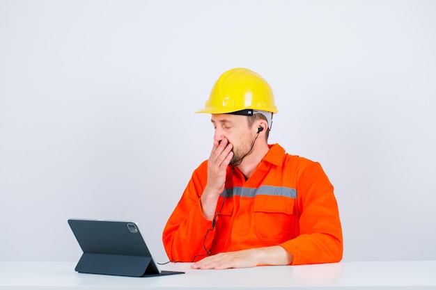 Young yawning engineer is holding his hand on mouth by sitting on white background