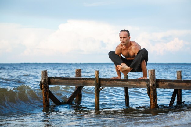 Young yoga trainer practicing yoga exercises on a wooden pier on a sea or river shore