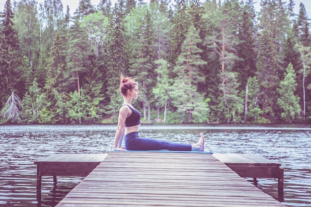 Young yogi girl practicing yoga sitting in Staff exercise Dandasana pose on the lake The concept of appeasement healthy lifestyle