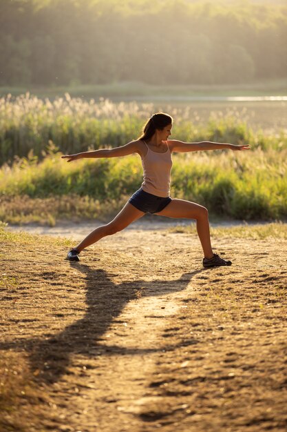 Young yogi woman doing exercises against the river and the forest.