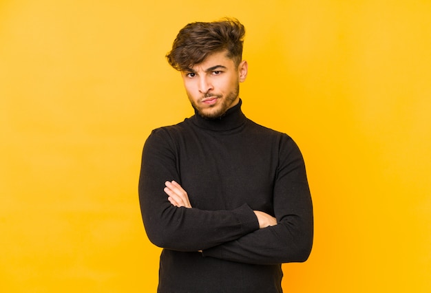 Youngian man isolated on a yellow wall frowning face in displeasure, keeps arms folded