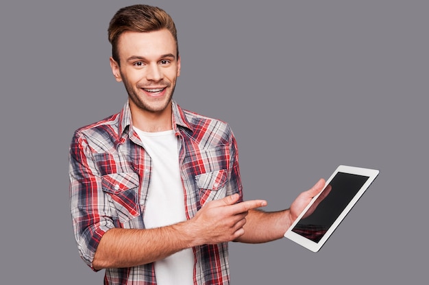 your advertisement may be here! cheerful young man holding a digital tablet and pointing it while standing against grey background