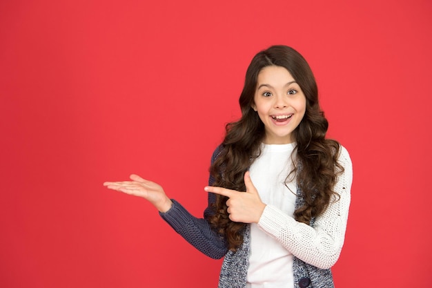 Your advertisement or promotional text happy kid pointing at\
red background advertising for product shopping girl show empty\
copy space product promotion showing direction pointing to\
product