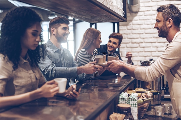 Your order is ready! Side view of barista passing coffee cups to his customer while standing at bar counter