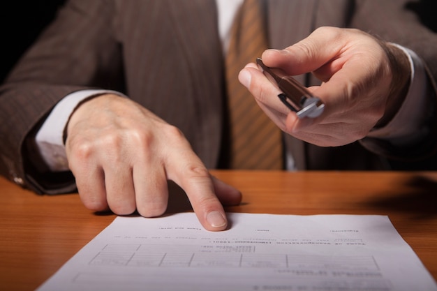 Photo your signature here! cropped image of man in formalwear giving a pen to you and pointing a document while isolated on black background