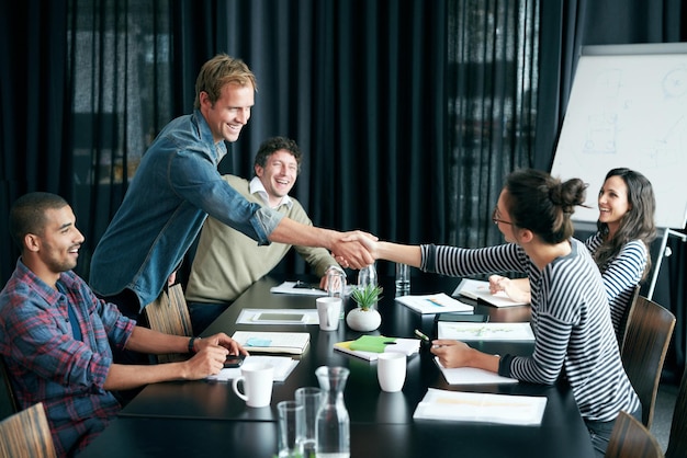 Youre going places in this company Shot of two colleagues shaking hands in a boardroom while coworkers look on