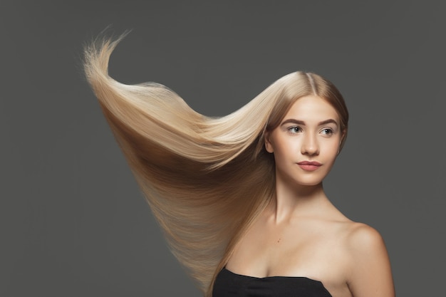 Youth Beautiful model with long smooth flying blonde hair on dark grey studio background