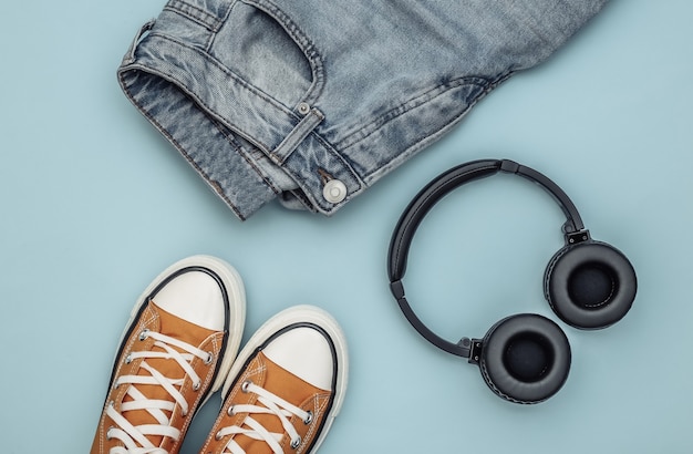 Youth clothing and accessories. Sneakers, jeans and headphones on blue background. Top view. Flat lay