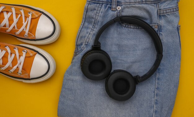 Youth clothing and accessories. Sneakers, jeans and headphones on a yellow background. Top view. Flat lay